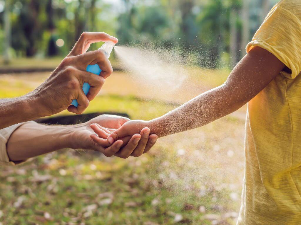 an adult spraying repellent on a kid